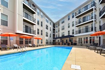 A swimming pool in front of apartment buildings with orange umbrellas.